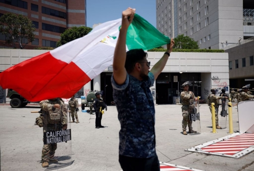 1名男子10 日高举墨西哥国旗,在洛杉矶市中心的加州国民警卫队成员面前抗议。路透社 1名男子10 日高举墨西哥国旗,在洛杉矶市中心的加州国民警卫队成员面前抗议。路透社