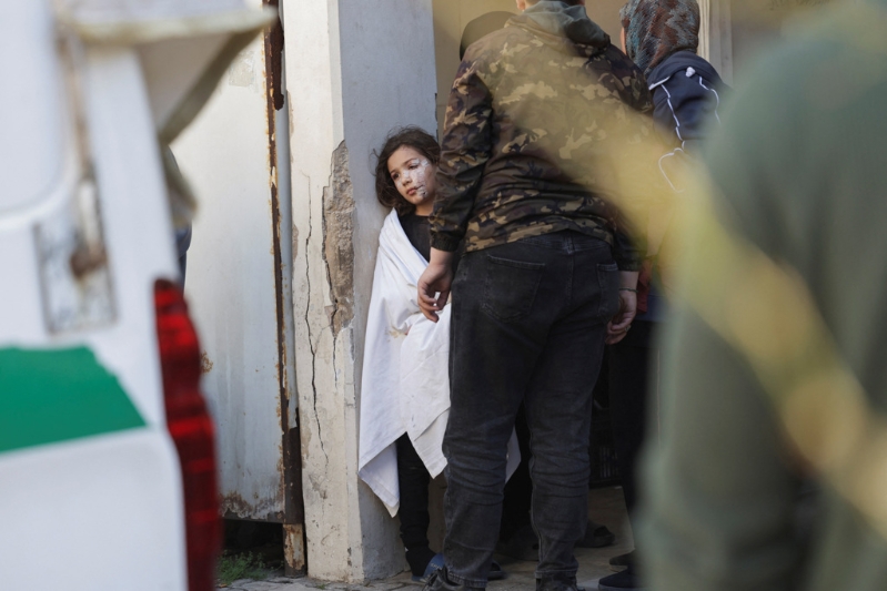 一名满脸是伤的女孩目睹救护员把她已身亡的父亲抬上车准备送去下葬的场面,神色茫然。 一名满脸是伤的女孩目睹救护员把她已身亡的父亲抬上车准备送去下葬的场面,神色茫然。